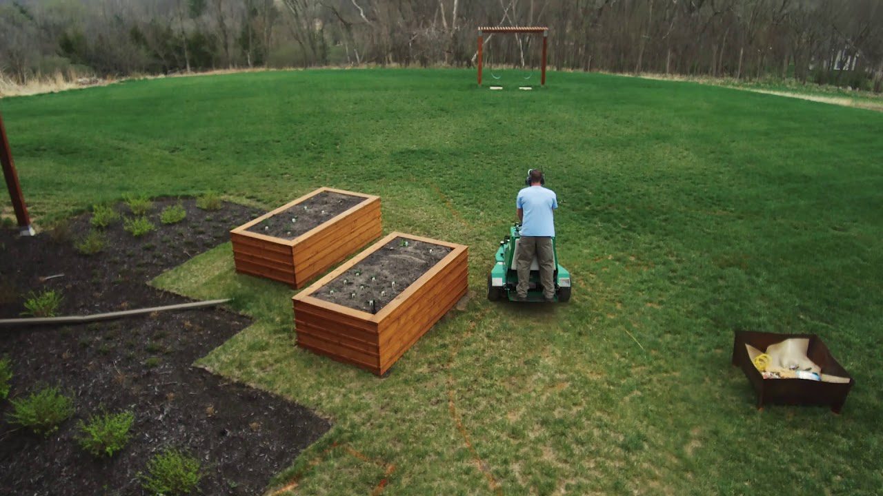 man operating a Ryan stand-on aerator next to raised gardening beds